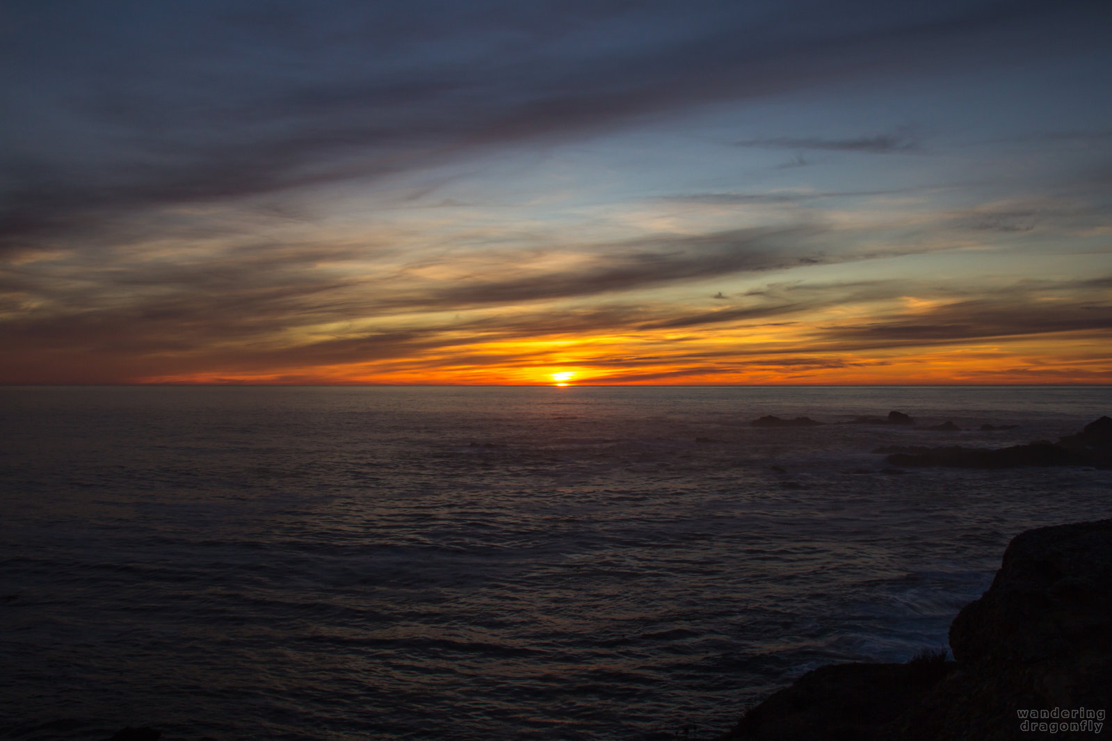 Last wink of the sun -- cloud, ocean, rock, sun, sunset, water, wave