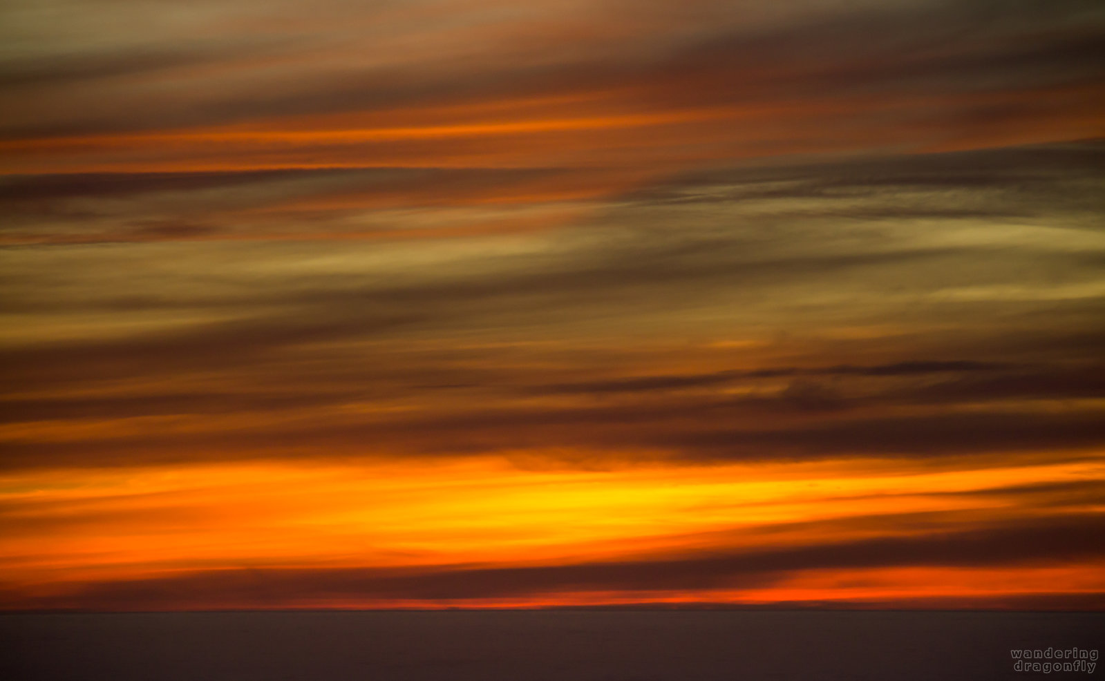 Striped sky above the dark ocean -- ocean, red, sunset, water, yellow